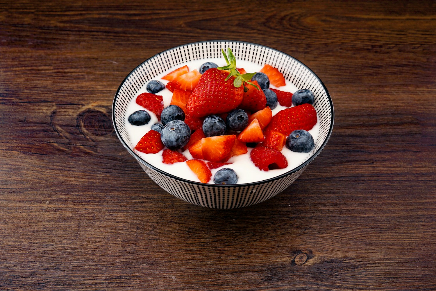 Yogurt topped with strawberries and blueberries in a patterned bowl on a wooden table.